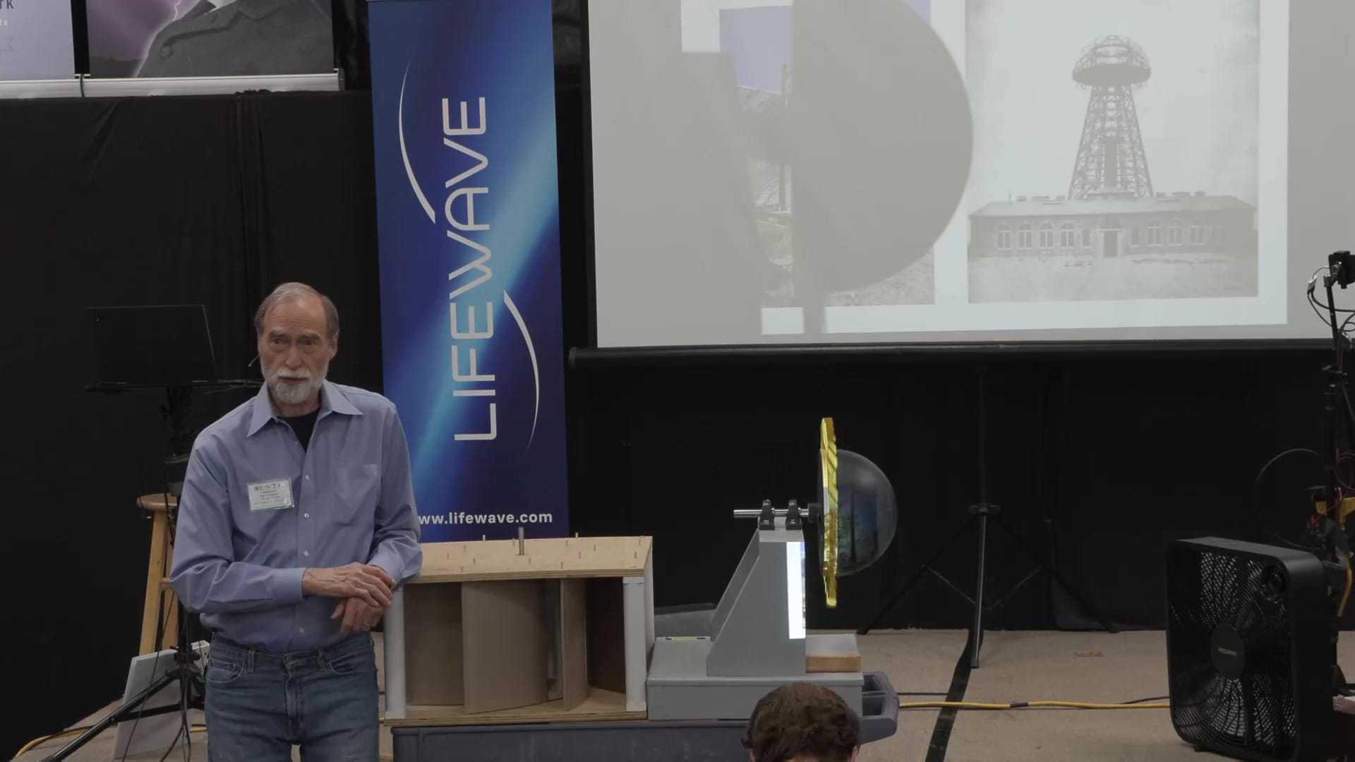 The sunflower turbine, Lindemann's horizontal-axis design with a foam-dome diverter and sheet-metal fins, on stage beside the box fan