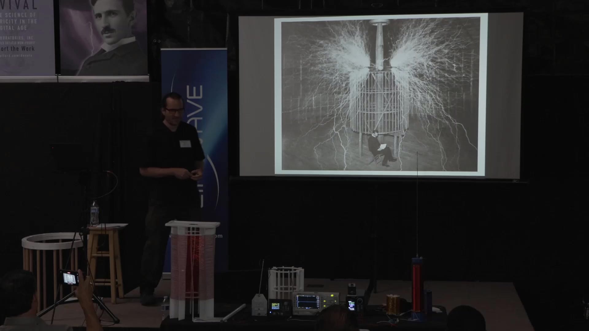 Tesla's Colorado Springs magnifying transmitter on screen, with the conference coils on the bench below