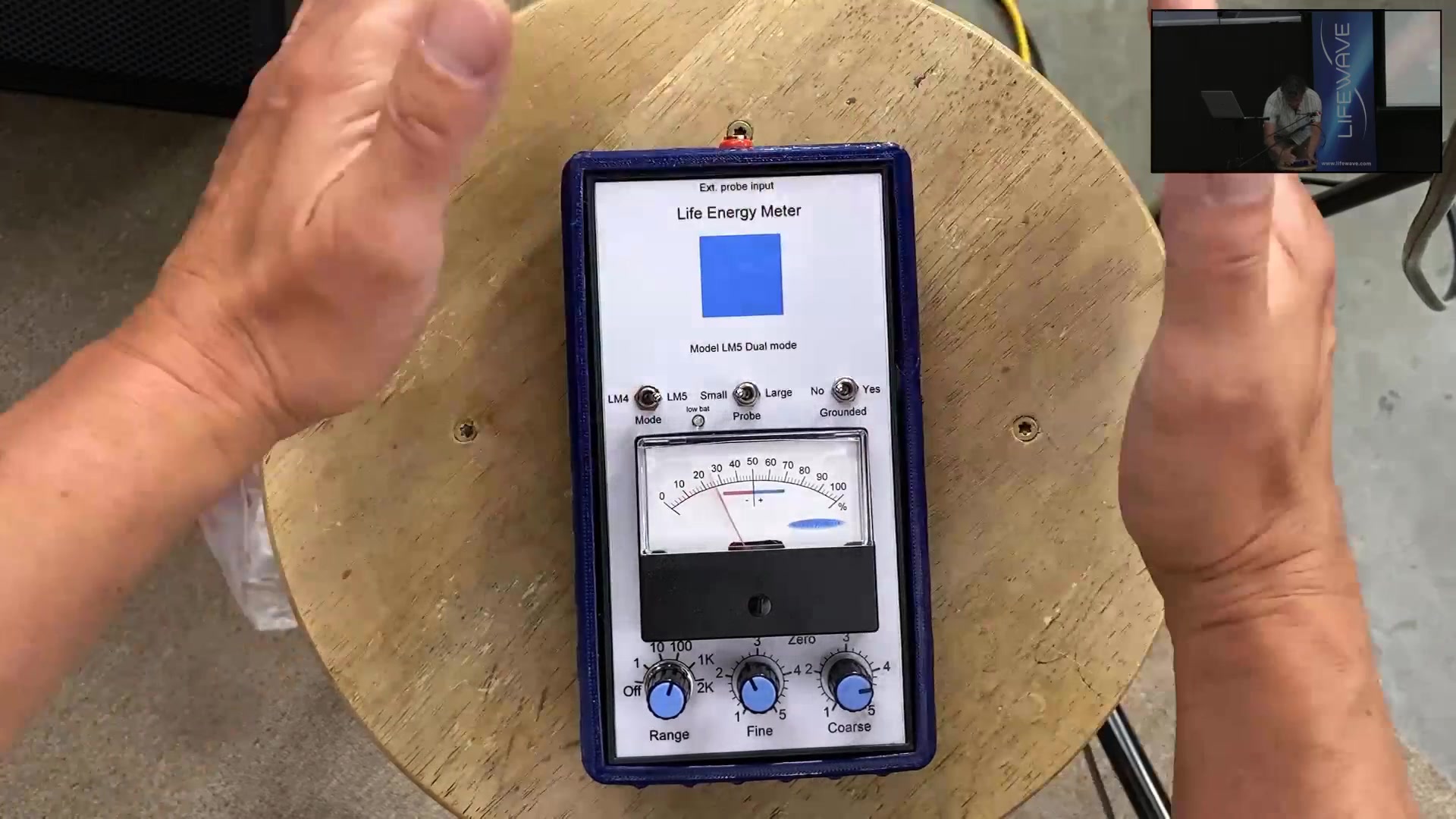 A handheld Life Energy Meter demonstrated on camera during the presentation